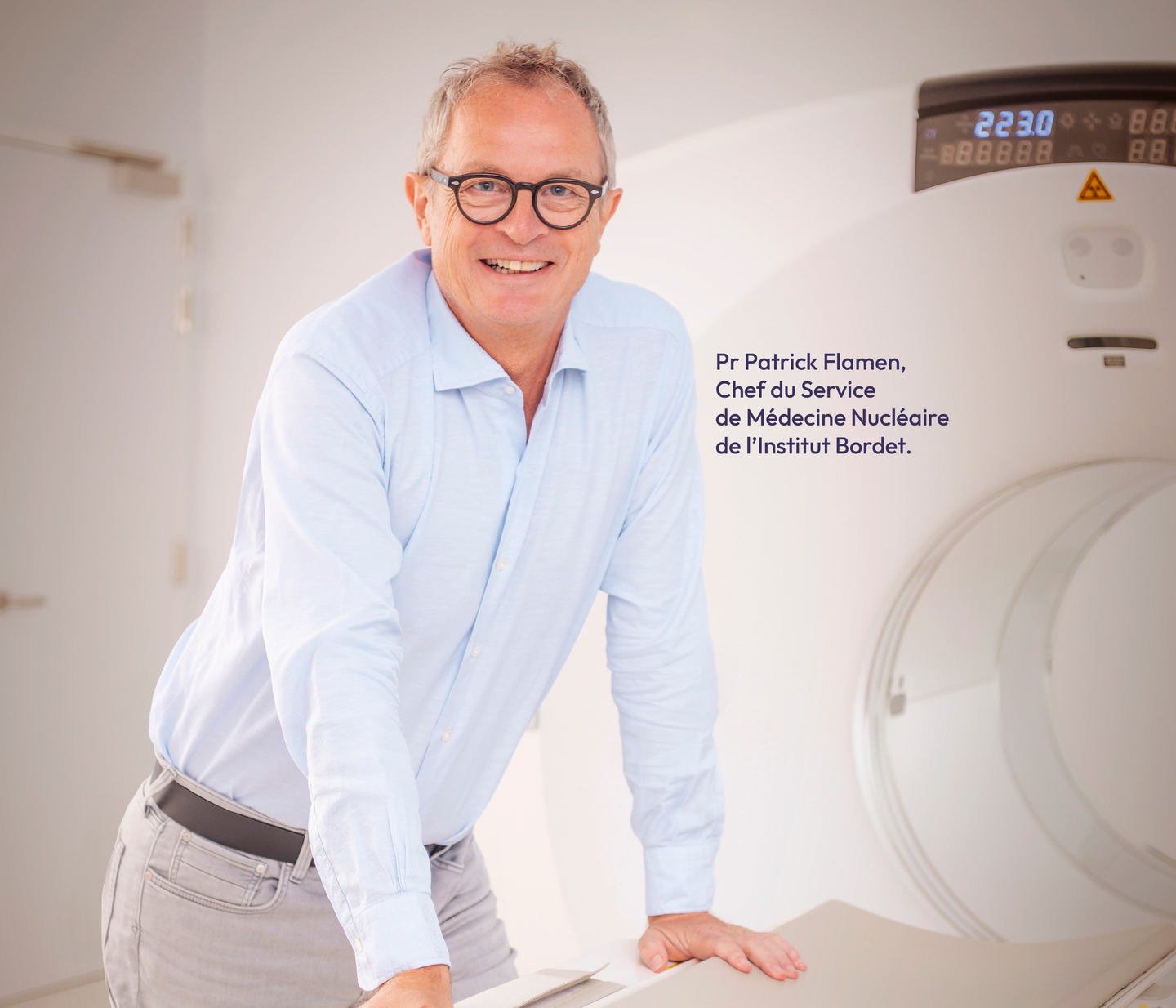 Pr Patrick Flamen en lunettes se positionne à côté d'une machine IRM, avec la mention : "Chef du Service de Médecine Nucléaire de l'institut Bordet".